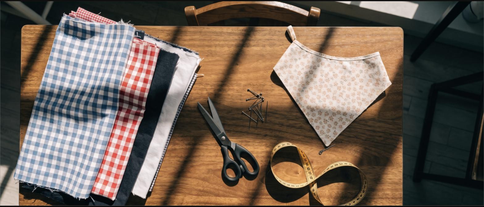 Folded cotton fabric, scissors, pins and a finished dog bandana on a wooden table